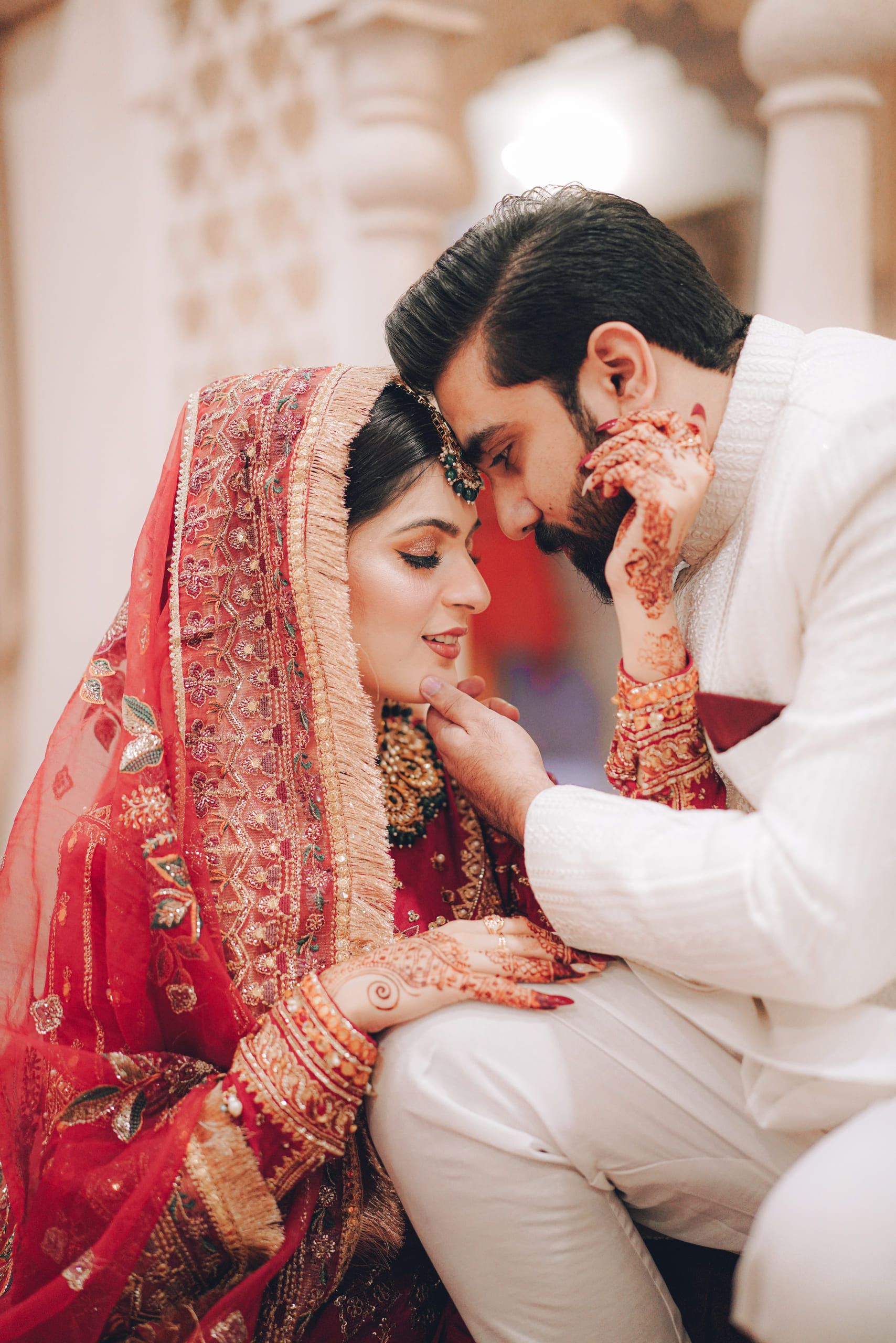 Bride in a red bridal lehenga in an intimate portrait with the groom, Lahore