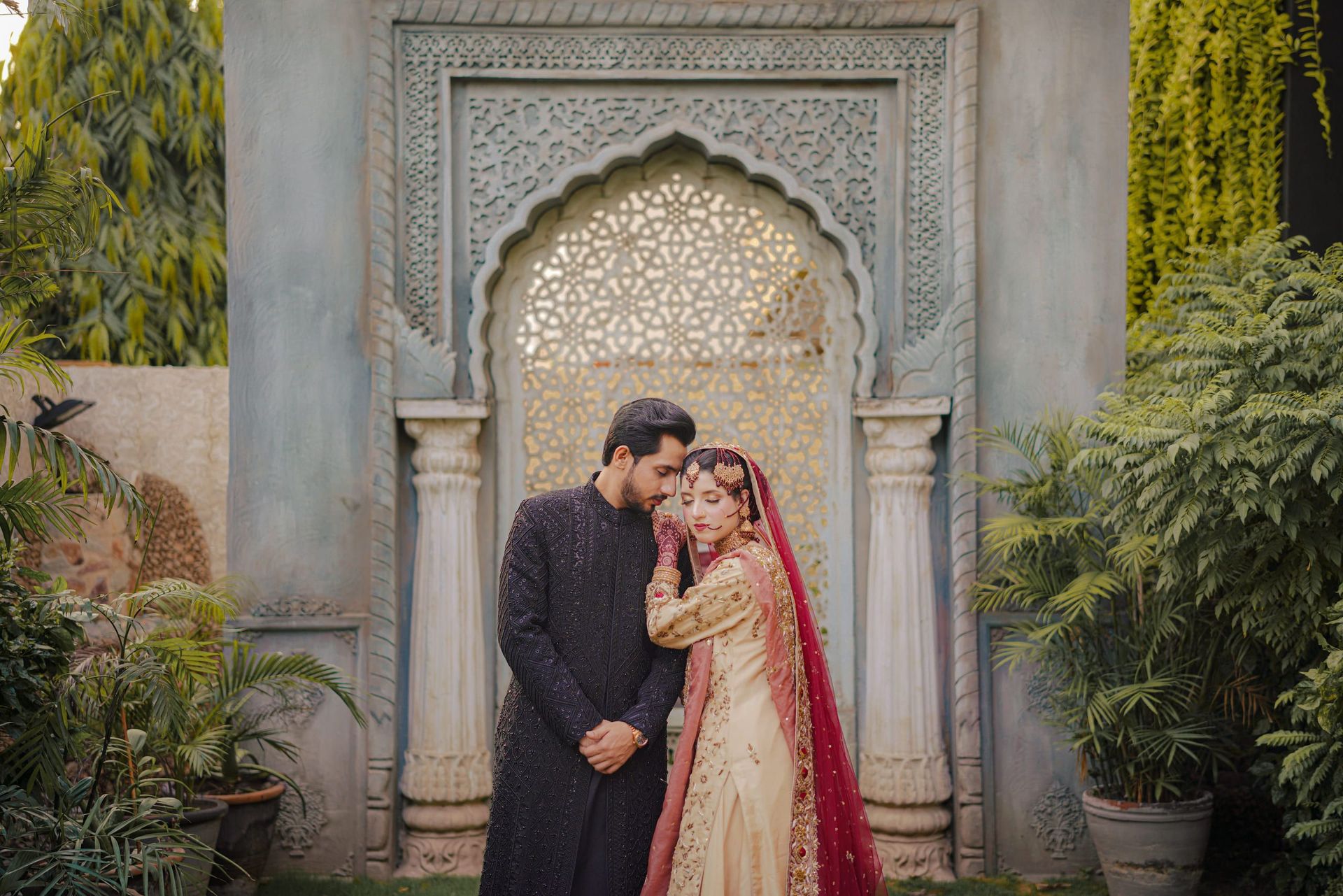 Couple before a carved white archway surrounded by greenery, Lahore wedding photography
