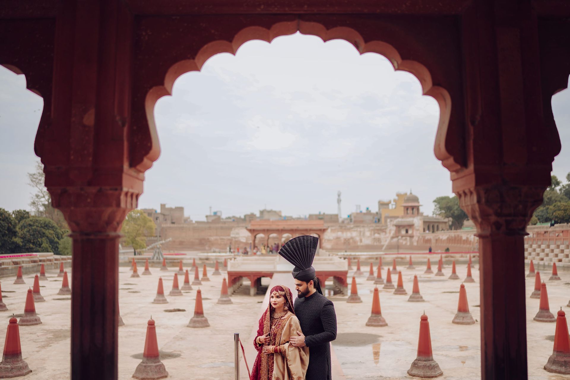 Bride and groom framed by the scalloped red sandstone arches of a Mughal courtyard in the Walled City, Lahore